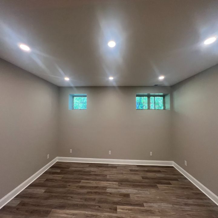 Empty finished room with gray walls, recessed ceiling lights, small windows, and wood-look flooring.