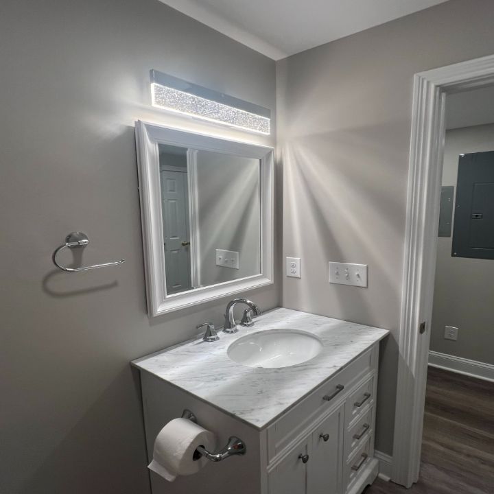 Modern bathroom vanity with marble countertop, mirror, wall light, and gray walls