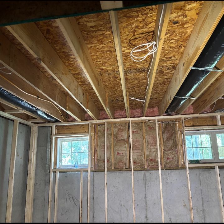 Unfinished room interior with exposed wall studs, ceiling joists, insulation, and two small windows.