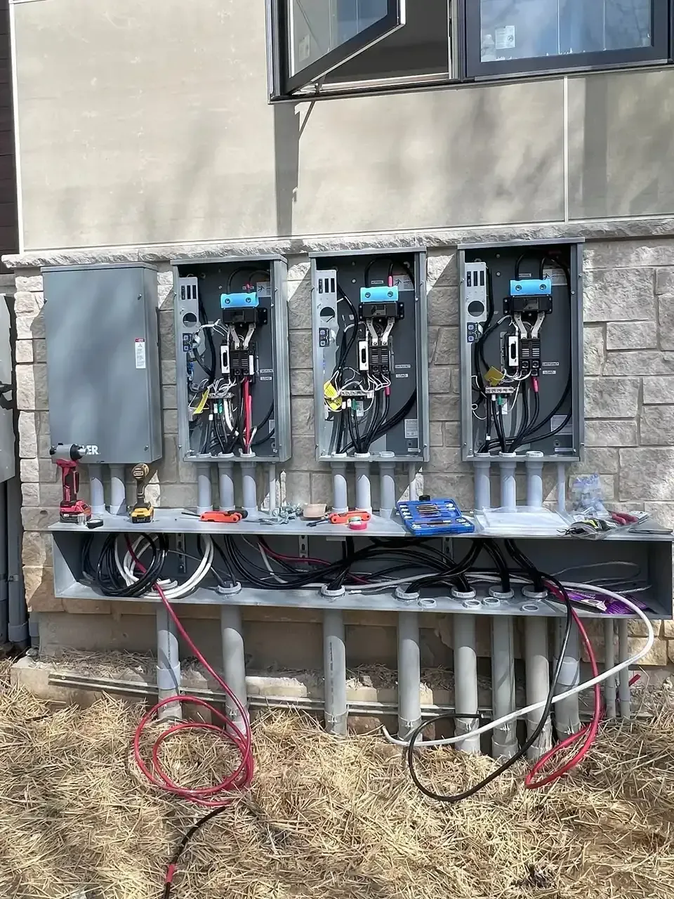 Electrical meter boxes mounted on a stone wall; wiring and tools in view.