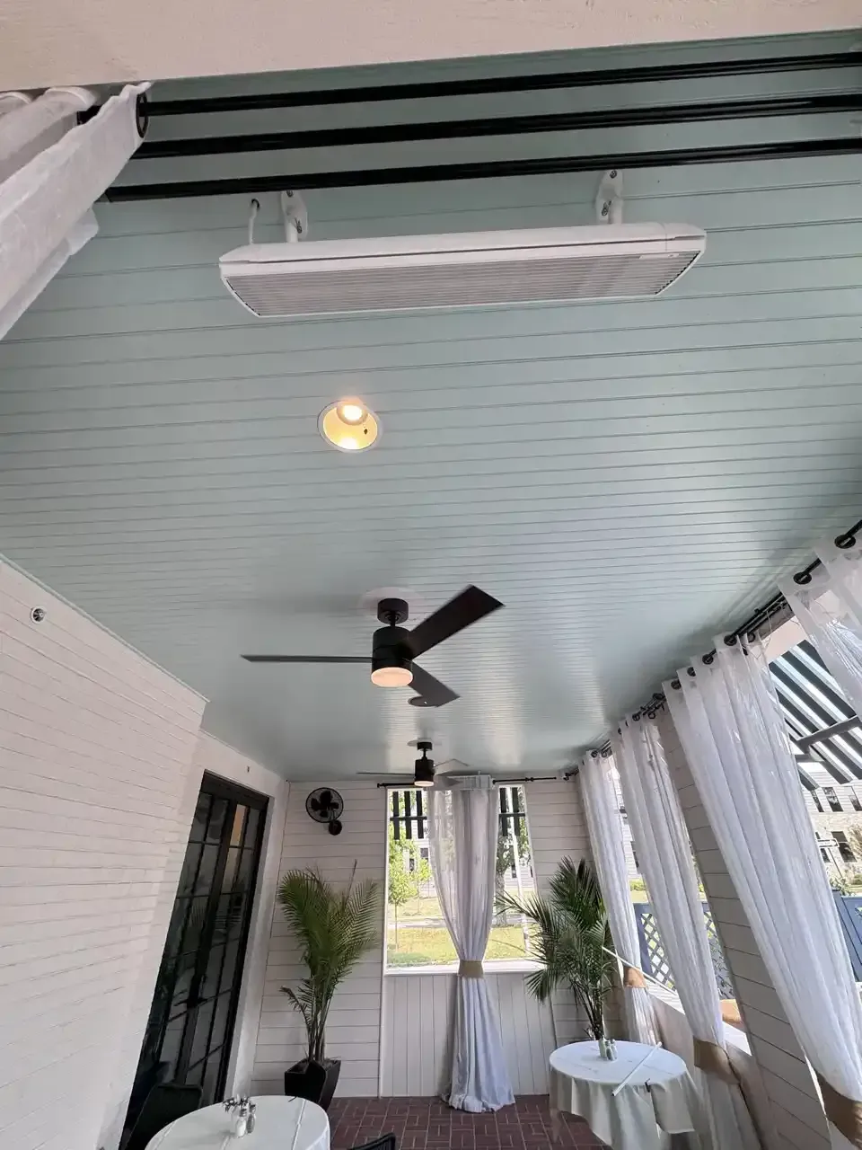 Covered porch ceiling with speakers, fan, and light fixtures; white curtains and aqua-painted planks.