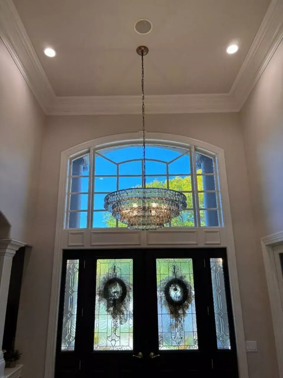 Entryway with chandelier, large arched window, double doors, two wreaths, recessed lighting.