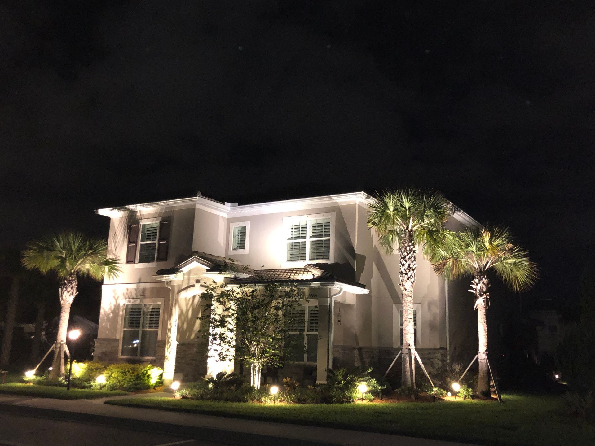 Illuminated two-story house at night with palm trees and landscaped front yard