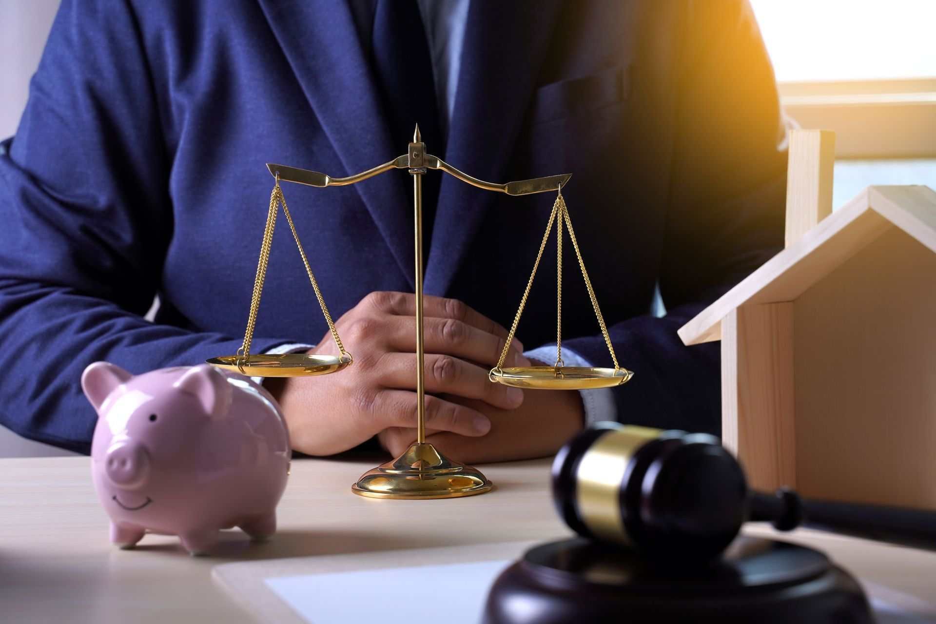 Scales of justice, gavel, house model, and piggy bank on desk, representing estate planning. Scales of justice, gavel, house model, and piggy bank on desk, representing estate planning.