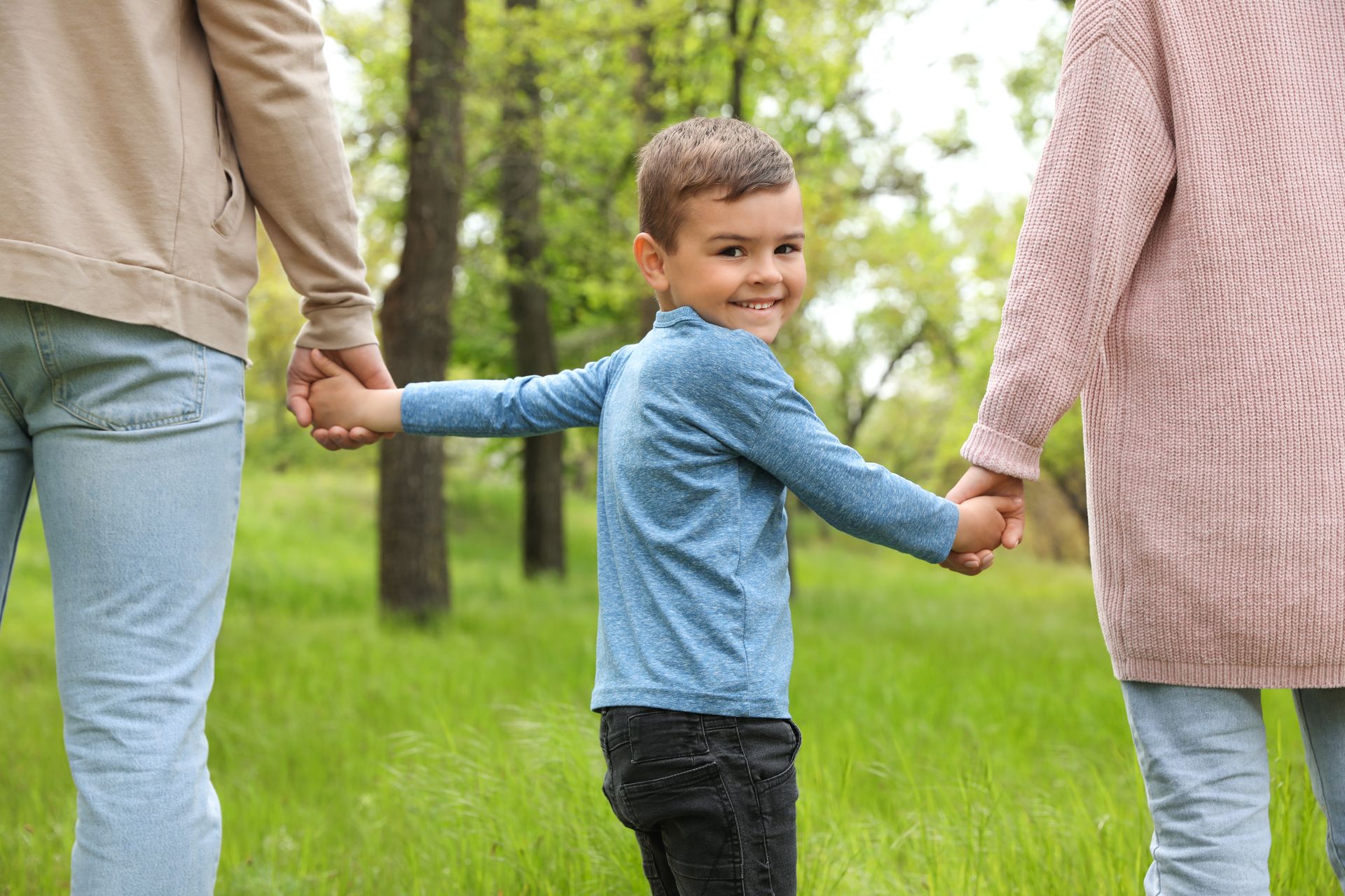 Smiling boy holding his parents' hands in a park, representing child custody