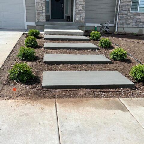 Front steps to a house with concrete pavers and small shrubs in a landscaped bed