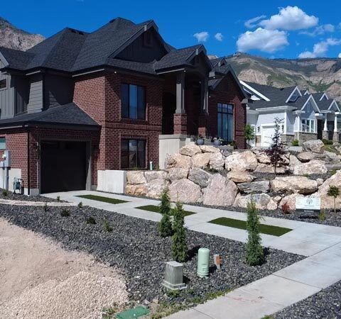 Modern brick house with landscaped yard, stone retaining wall, and mountain backdrop