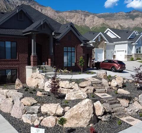 Suburban brick house with landscaped rock garden and a red car in the driveway under a blue sky