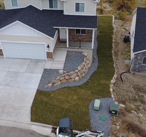 Aerial view of a house with a new concrete driveway, stone-lined front path, and sloped grassy yard
