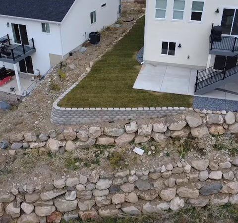 Aerial view of white houses beside a stone retaining wall and grassy yard near stairs and patios
