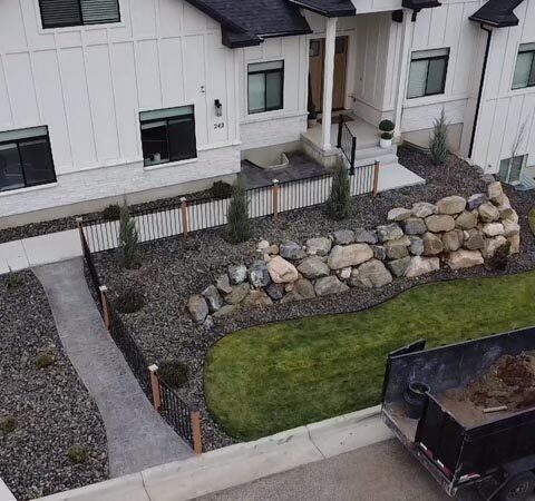 Front yard with rock retaining wall, gravel path, green lawn, and white house exterior.