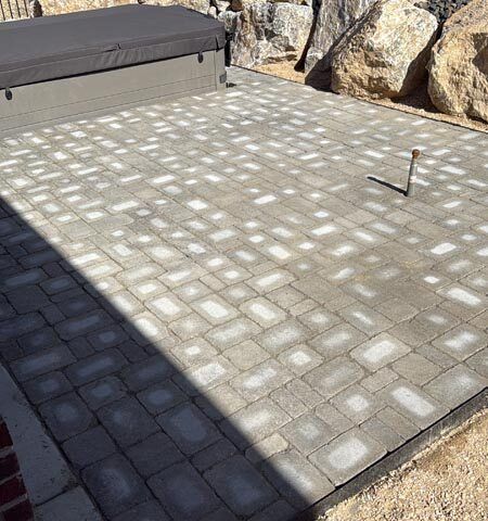 Paver patio with a small metal stake, bordered by rocks and a cushioned bench.