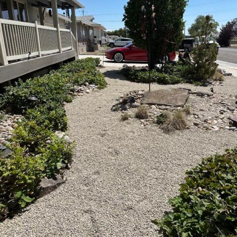 Gravel path beside a porch and rock garden, with a red car parked in the background.