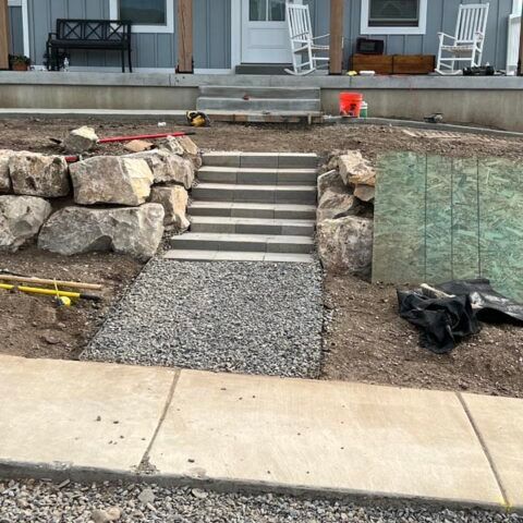 Front yard with stone retaining walls, central concrete steps, and gravel path leading to a house porch.