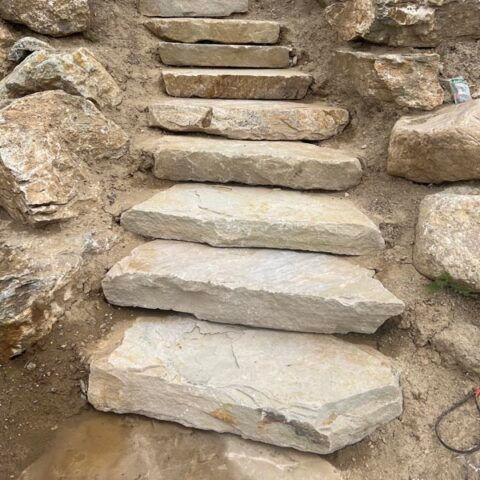 Rough stone steps built into a rocky hillside, leading upward between large boulders.