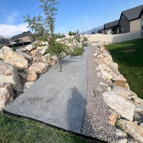 Concrete walkway through landscaped rocks in a suburban yard under a blue sky
