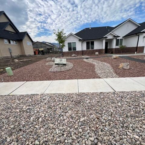 New home front yard with red gravel landscaping and a curved stone path under a cloudy sky