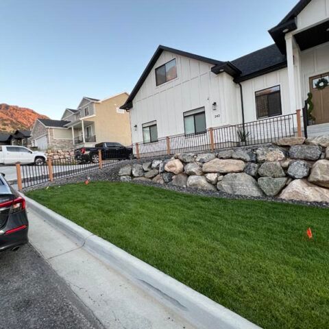Suburban homes beside a sloped green lawn and stone retaining wall at dusk