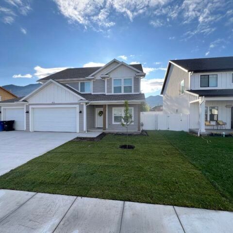 Suburban two-story house with a white garage, green lawn, and blue sky on a quiet street