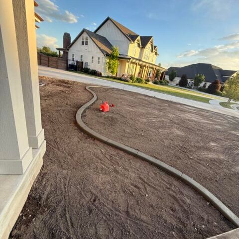 New house with dirt front yard, curved hose, and a red sprinkler at sunset