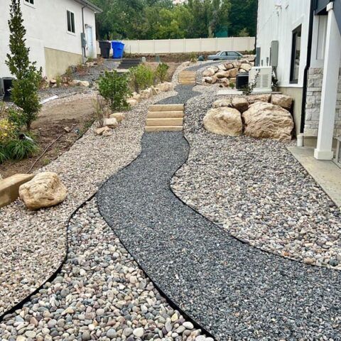 Curved gravel garden path with stone steps between two white houses and large landscape rocks