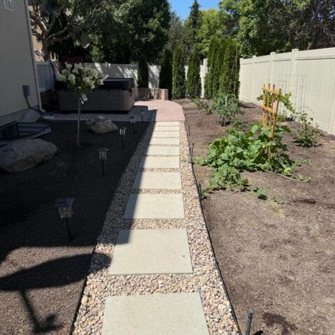 Backyard garden path with stepping stones beside raised beds and a white fence