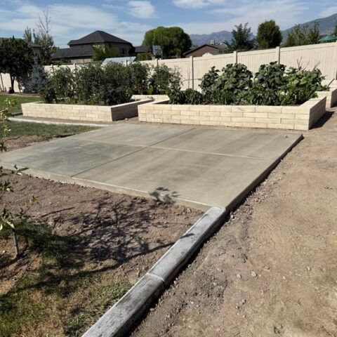 Concrete patio slab beside raised stone garden beds in a sunny backyard