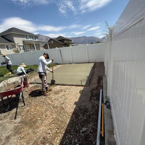 Worker smoothing fresh concrete slab in a fenced backyard on a sunny day