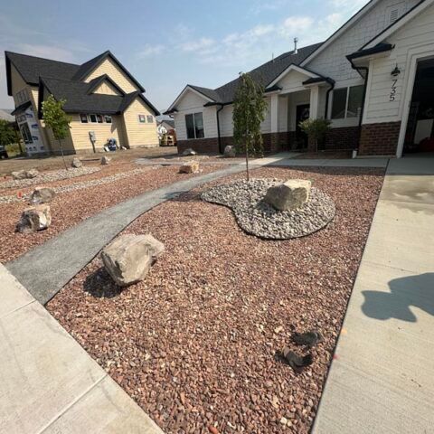 Modern residential landscaping with red gravel, large rocks, and curved concrete walkways between houses