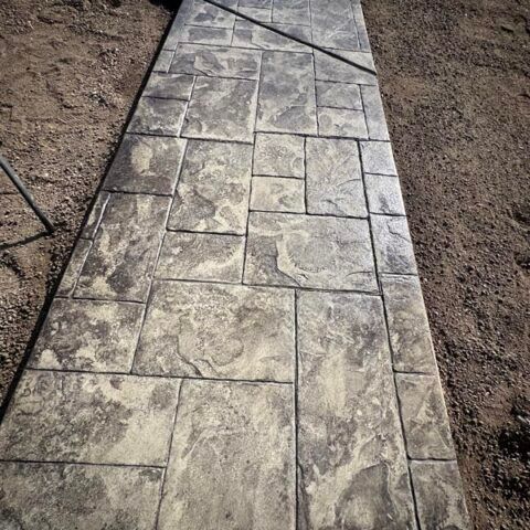 Stamped concrete walkway bordered by soil, with a diagonal seam near the top.