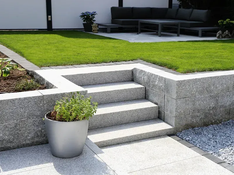 Modern patio with gray stone steps, a green lawn, and a potted plant in the foreground.