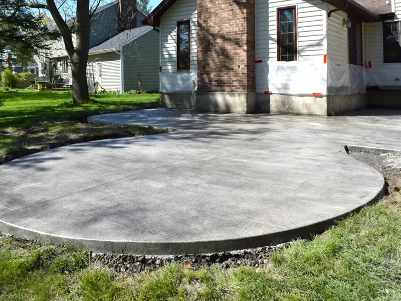 Round concrete patio beside a brick house, with a low curb and grass around it.