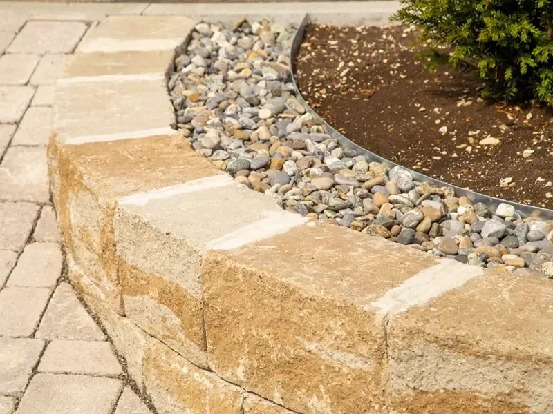 Curved tan stone retaining wall beside a paved walkway and decorative rock garden.