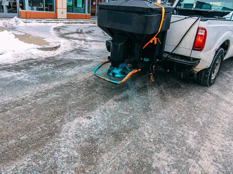 Pickup truck with salt spreader parked on a snowy lot near a building
