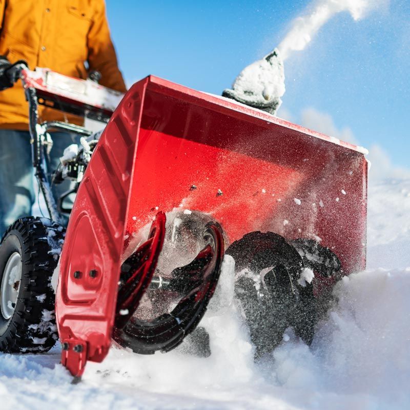 Red snow blower clearing deep snow outdoors, spraying white powder against a blue sky.