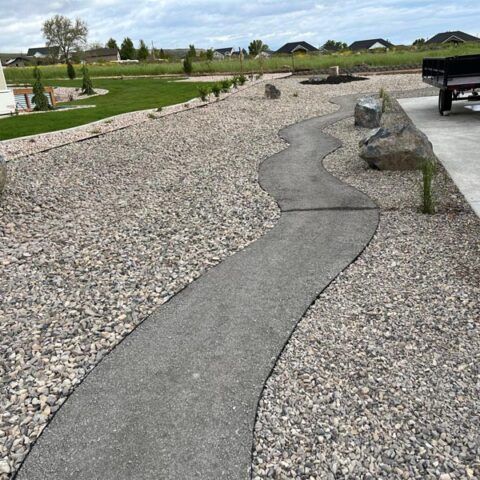 Winding concrete path through a gravel landscape beside a driveway and truck