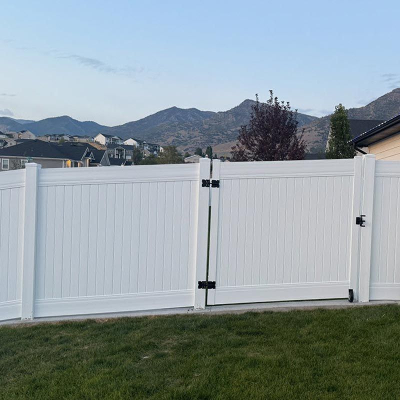 White vinyl fence with a central gate in a backyard, with mountains and houses in the distance.