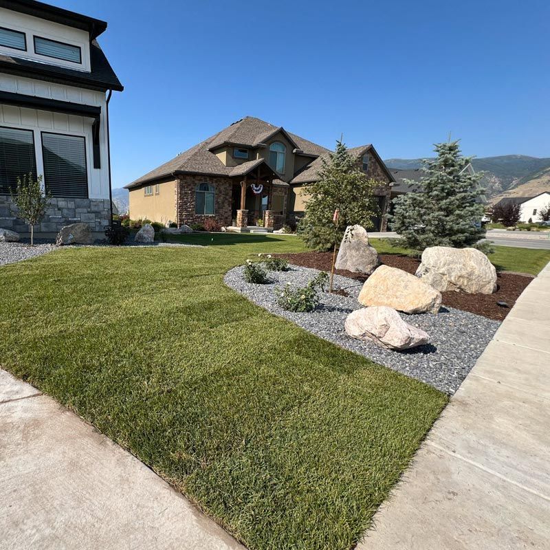 Suburban home with landscaped front yard, rock garden, and concrete driveway under a clear blue sky