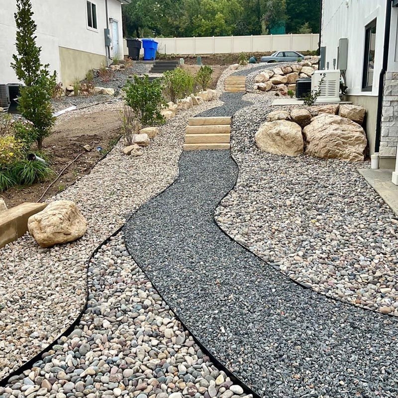 Gravel garden path between houses with rocks, shrubs, and small steps leading uphill