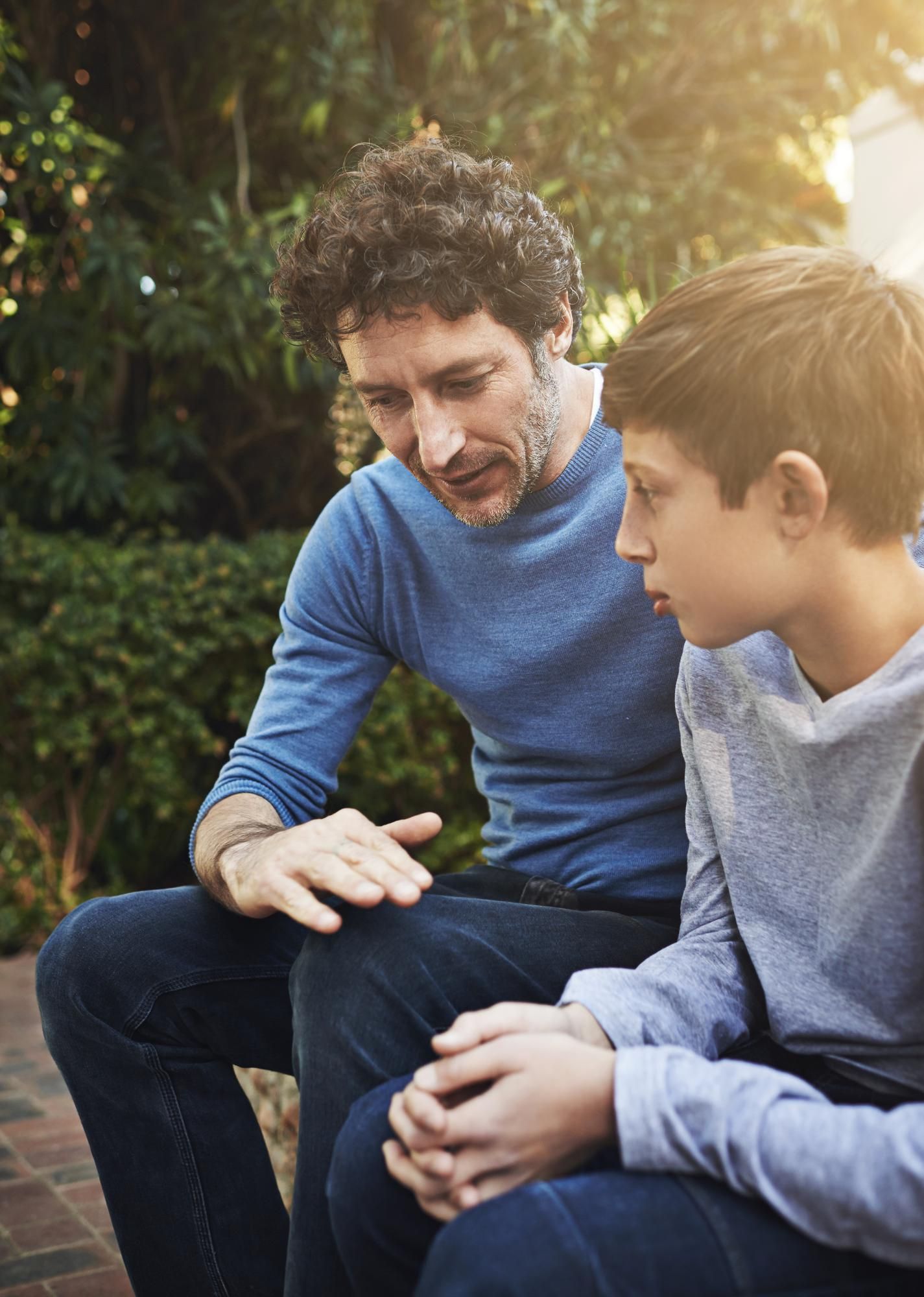 A man is sitting next to a young boy and talking to him.