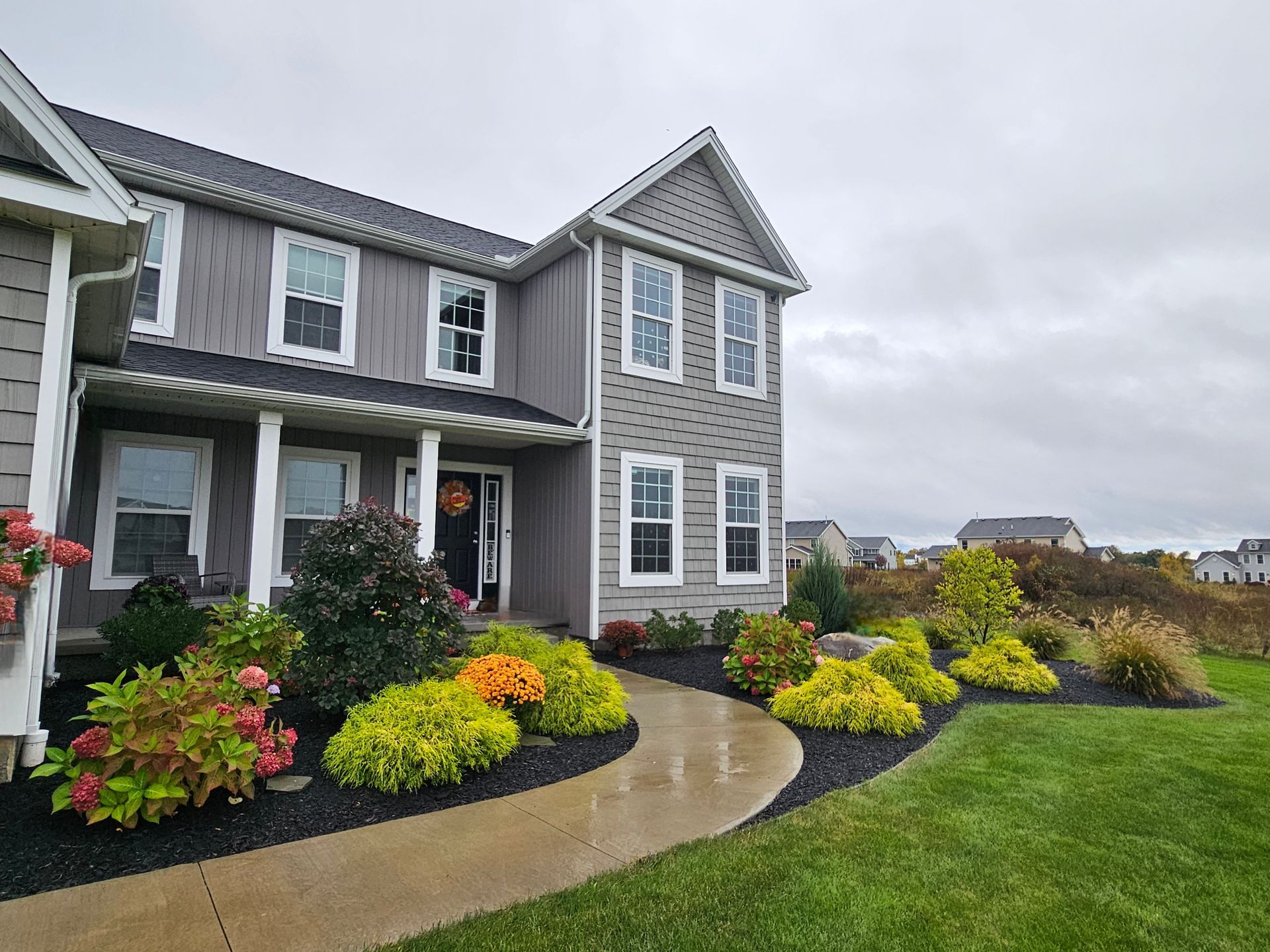 Lush green lawn with a winding gravel path, bordered by trees and shrubs, leading to a house.
