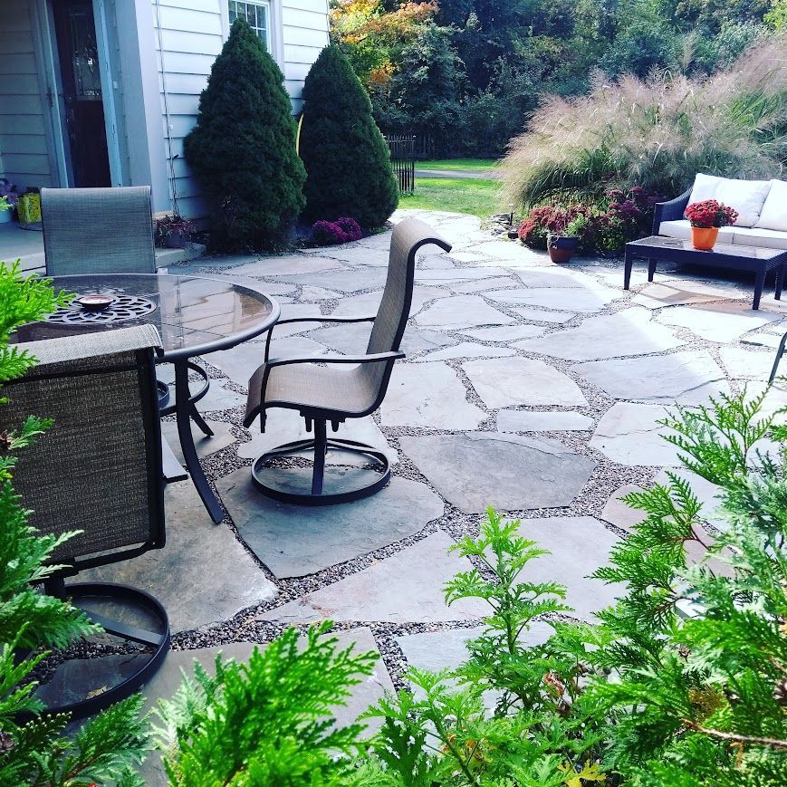 Stone patio with outdoor furniture surrounded by landscaping.