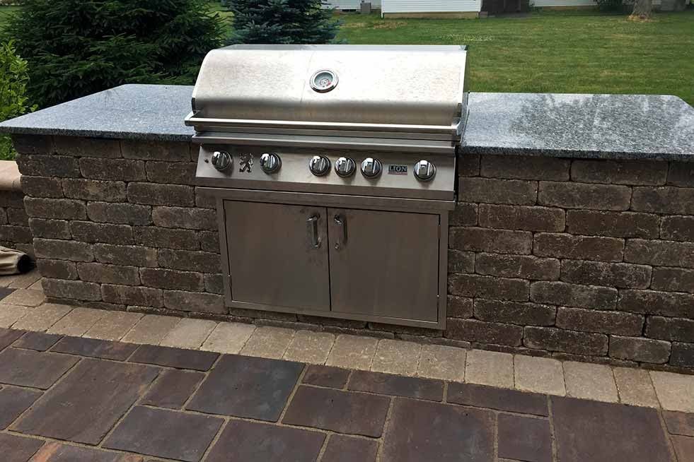 Built-in outdoor stainless steel grill on a brick and granite countertop island on a patio.