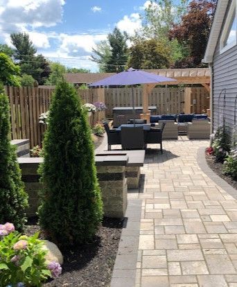 Backyard with lit hot tub, stone pathway, lawn, and surrounding trees, at dusk.
