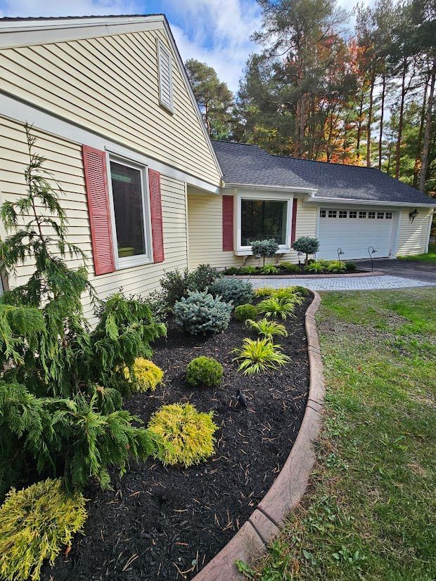 Garden bed with dark mulch, various green plants, and black post lights against a lush lawn.