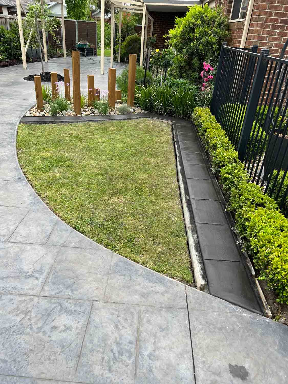 A concrete walkway leading to a lush green lawn with a fence in the background