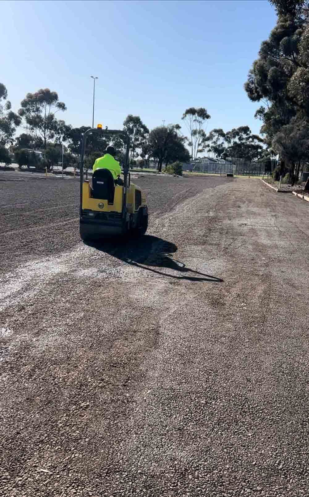 A man is driving a roller on a gravel road