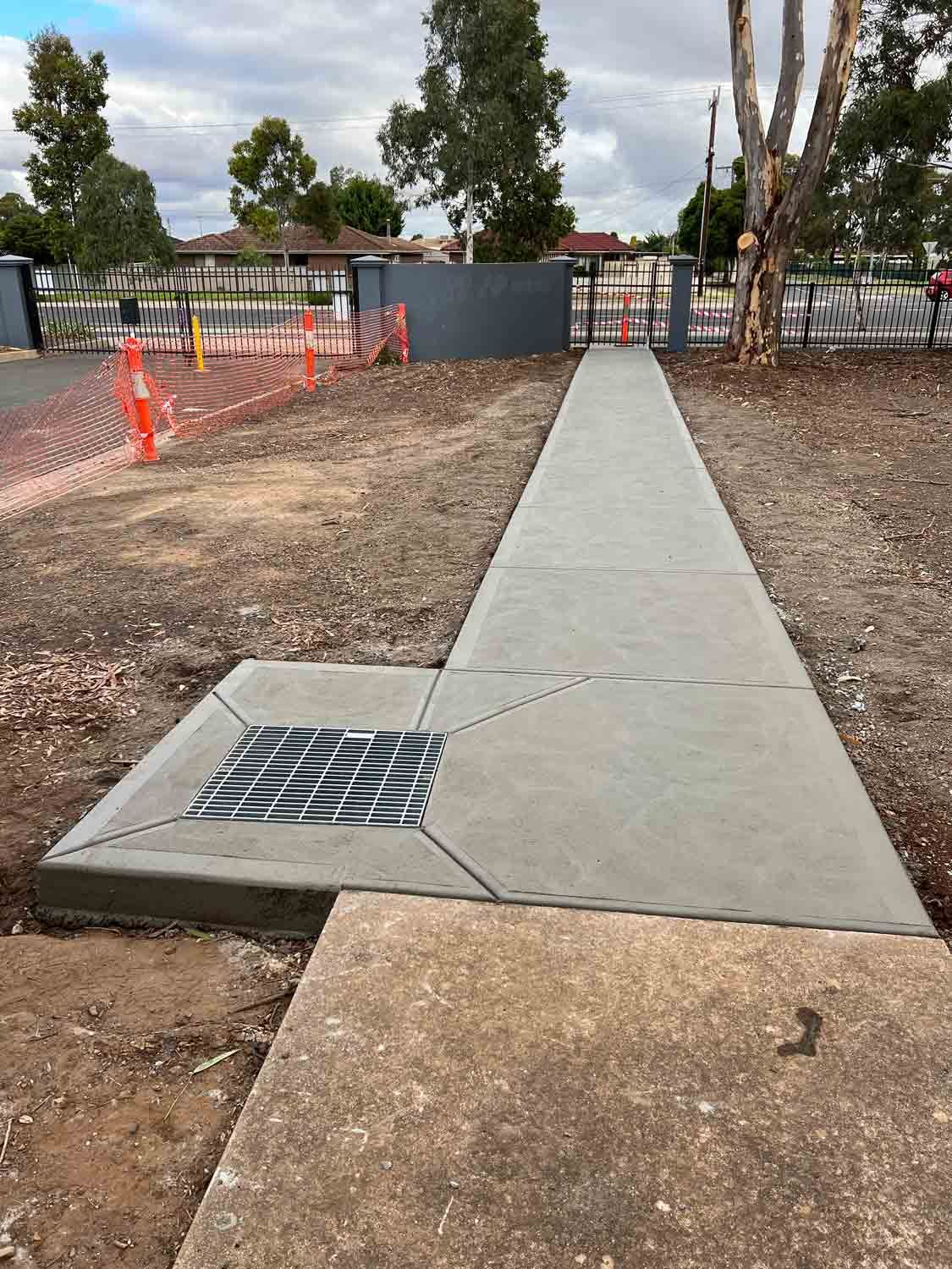 A concrete walkway with a metal grate on the side of it