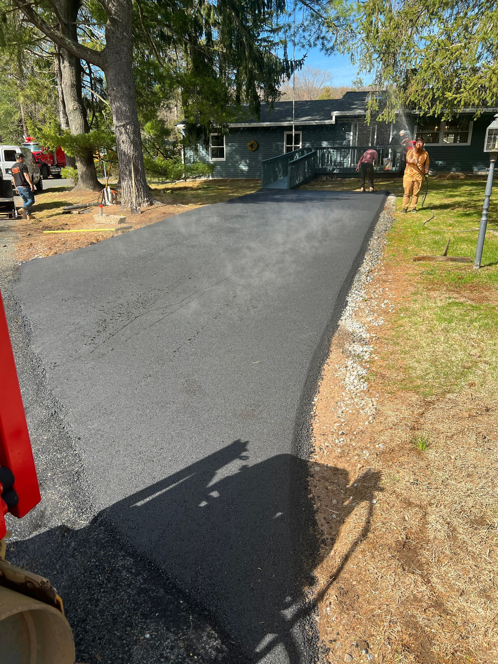 Newly paved asphalt driveway leading toward a green house with a small ramp, person standing to the side.
