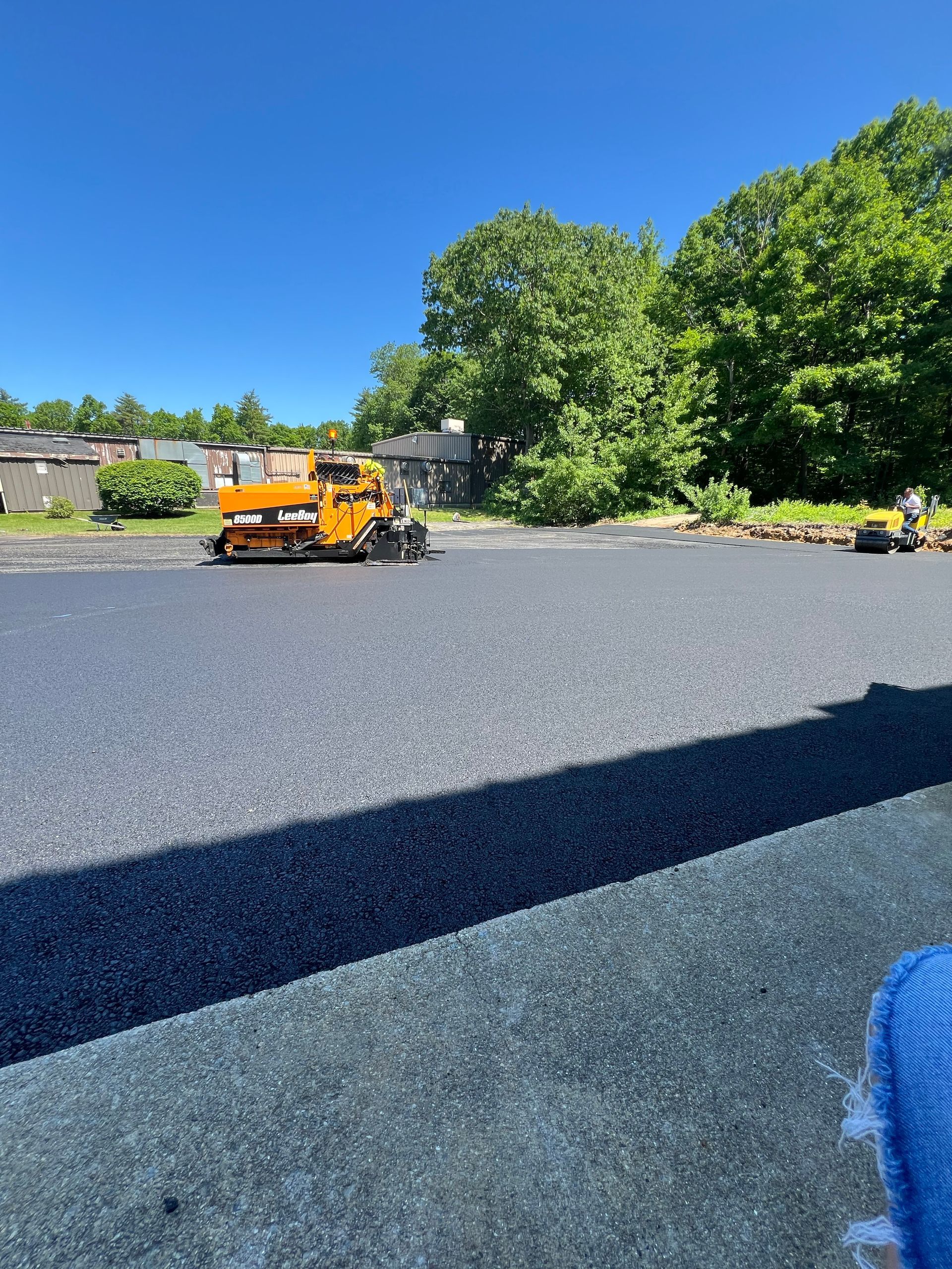 An orange asphalt paving machine laying fresh blacktop on a sunny day.